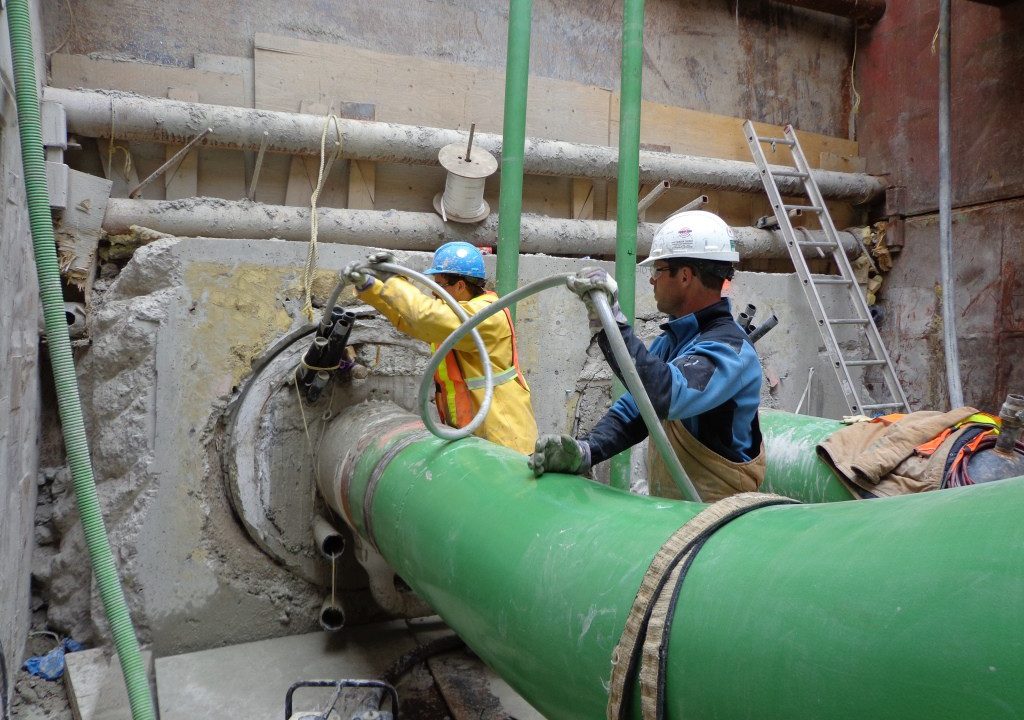 Crew grouting the annular space around a carrier pipe where it enters the host casing