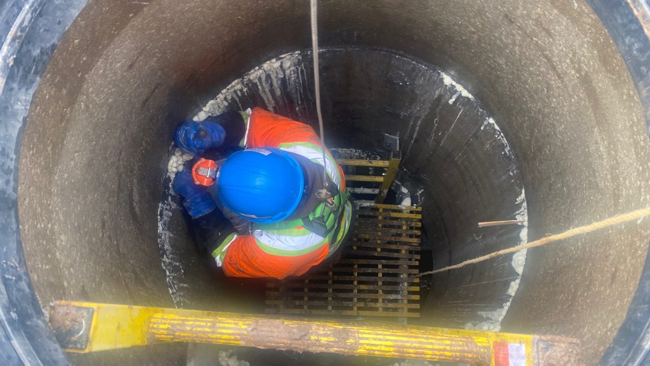 Harnessed technician working inside a manhole during a confined space grouting repair