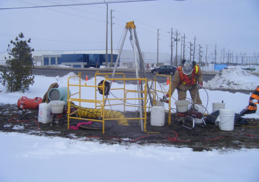 Confined space entry setup with tripod, retrieval equipment, and ventilation on a winter job site