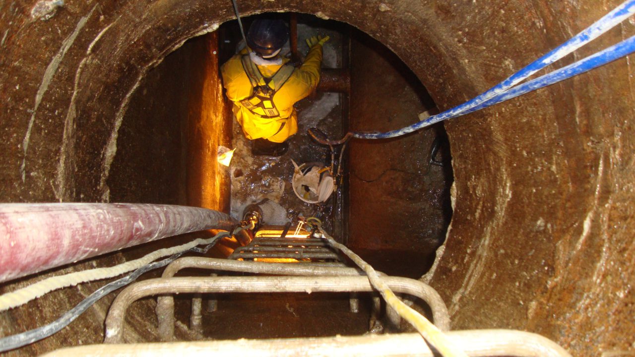 Technician on a manhole ladder running injection lines during municipal manhole rehabilitation