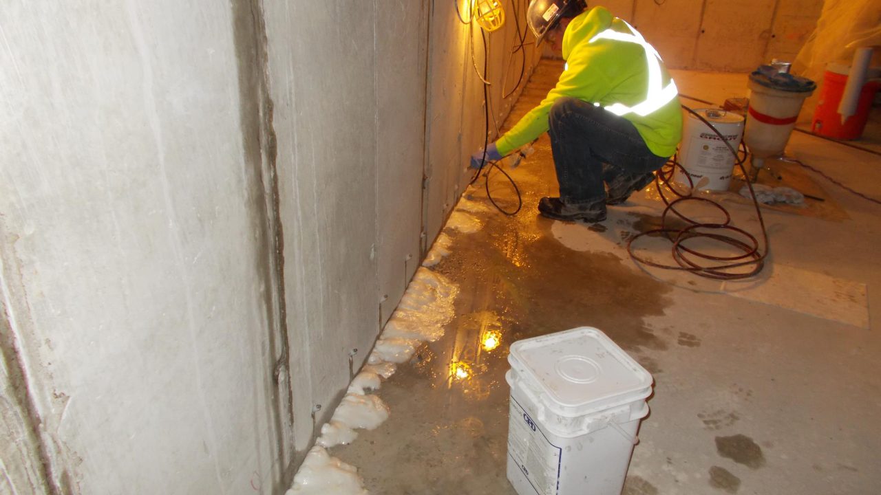Technician injecting polyurethane grout along a leaking concrete wall joint