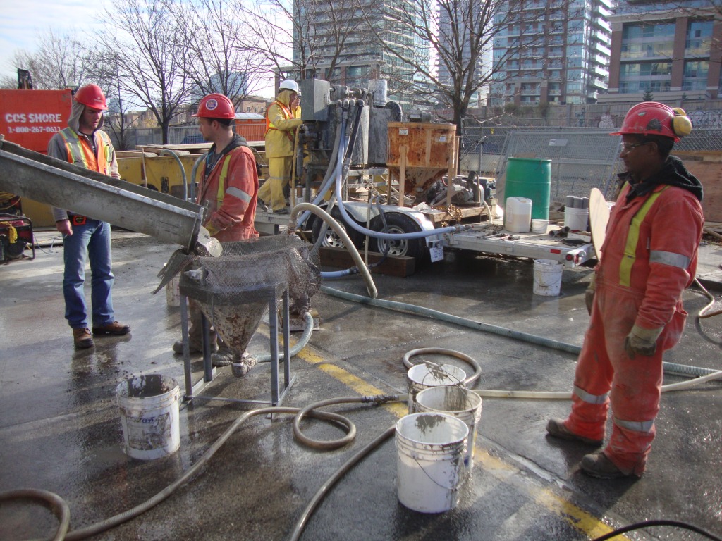 Crew pumping grout from a mixer on the street with ready-mix trucks behind