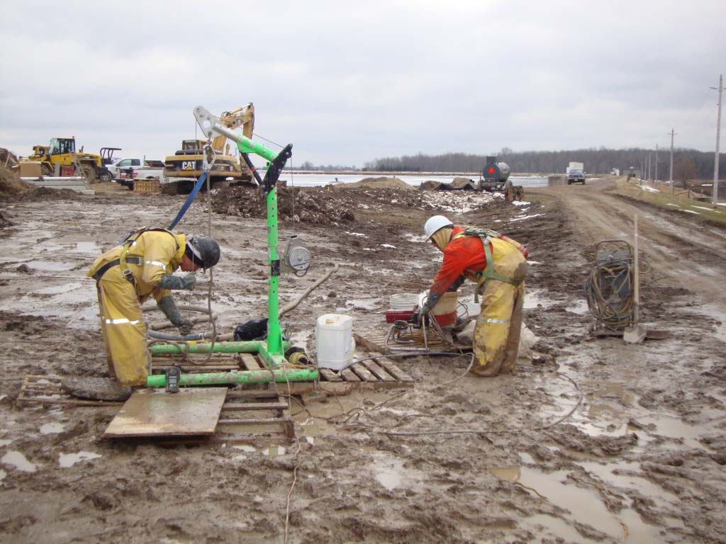 SG Services crew preparing injection equipment beside a manhole on an open construction site