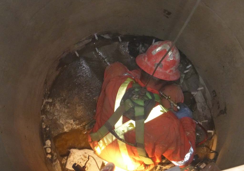 Harnessed technician injecting a leaking manhole joint inside a City of Waterloo sanitary manhole